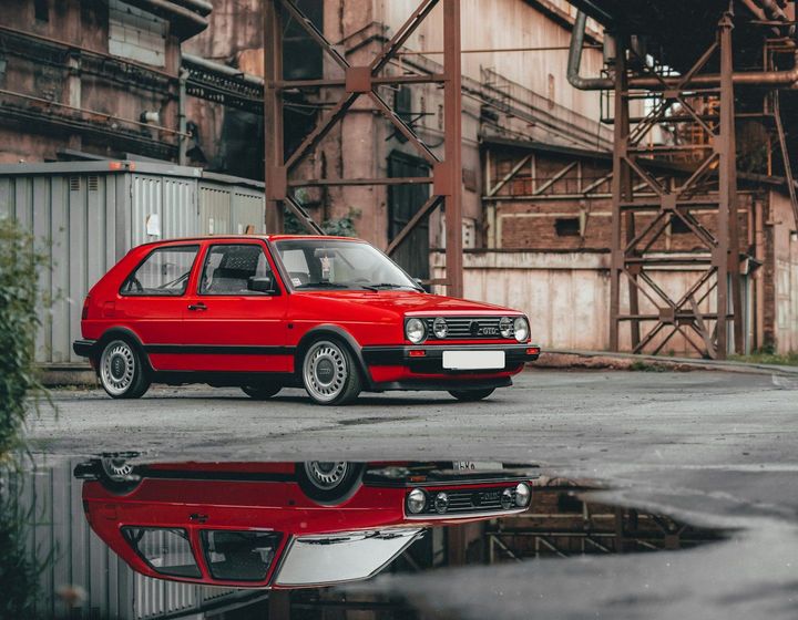 Czerwony hatchback zaparkowany na placu — auto starsze, wciąż w codziennym użytku